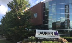 Wilfrid Laurier University building signage and academic co-op building in background with trees and shrubbery